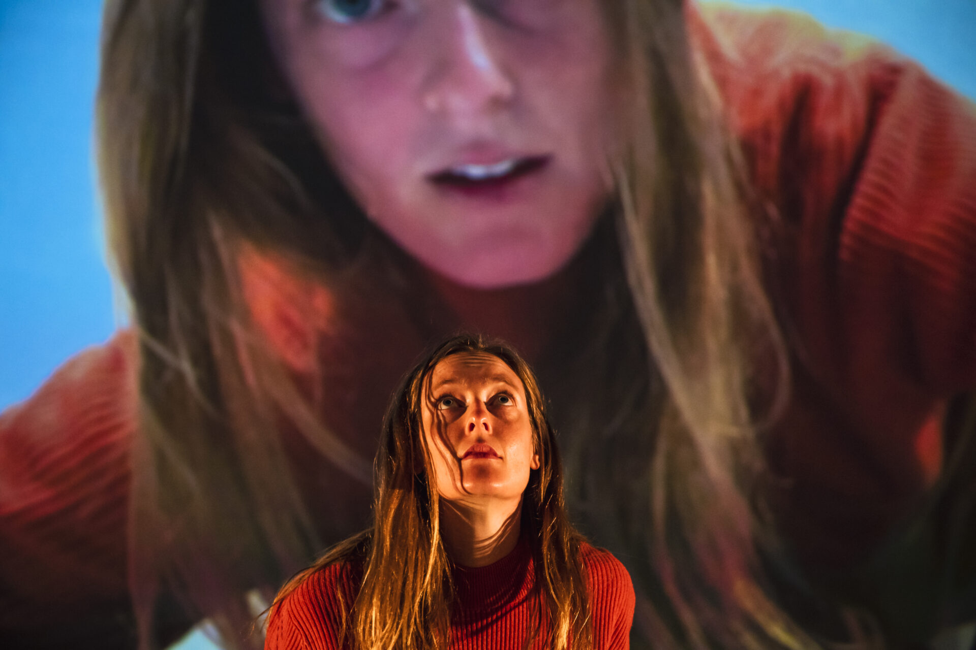 Young female dancer looking up. Behind her is a larger projection of herself