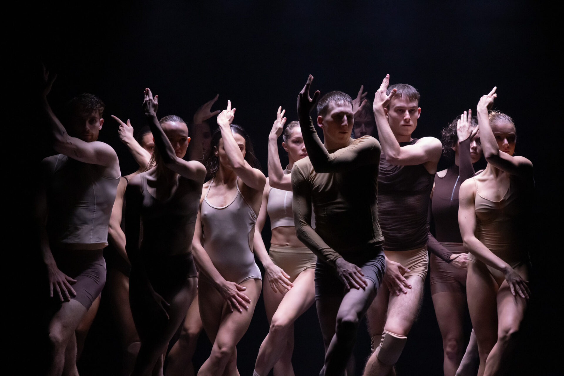 Sydney Dance Company dancers move in unison on stage, with their arms partially covering their face.