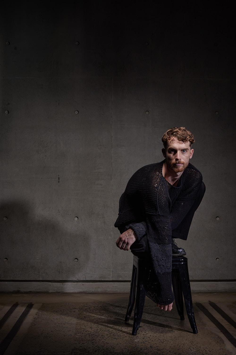 Company Dancer Dean Elliot sits on a chair dressed in black.